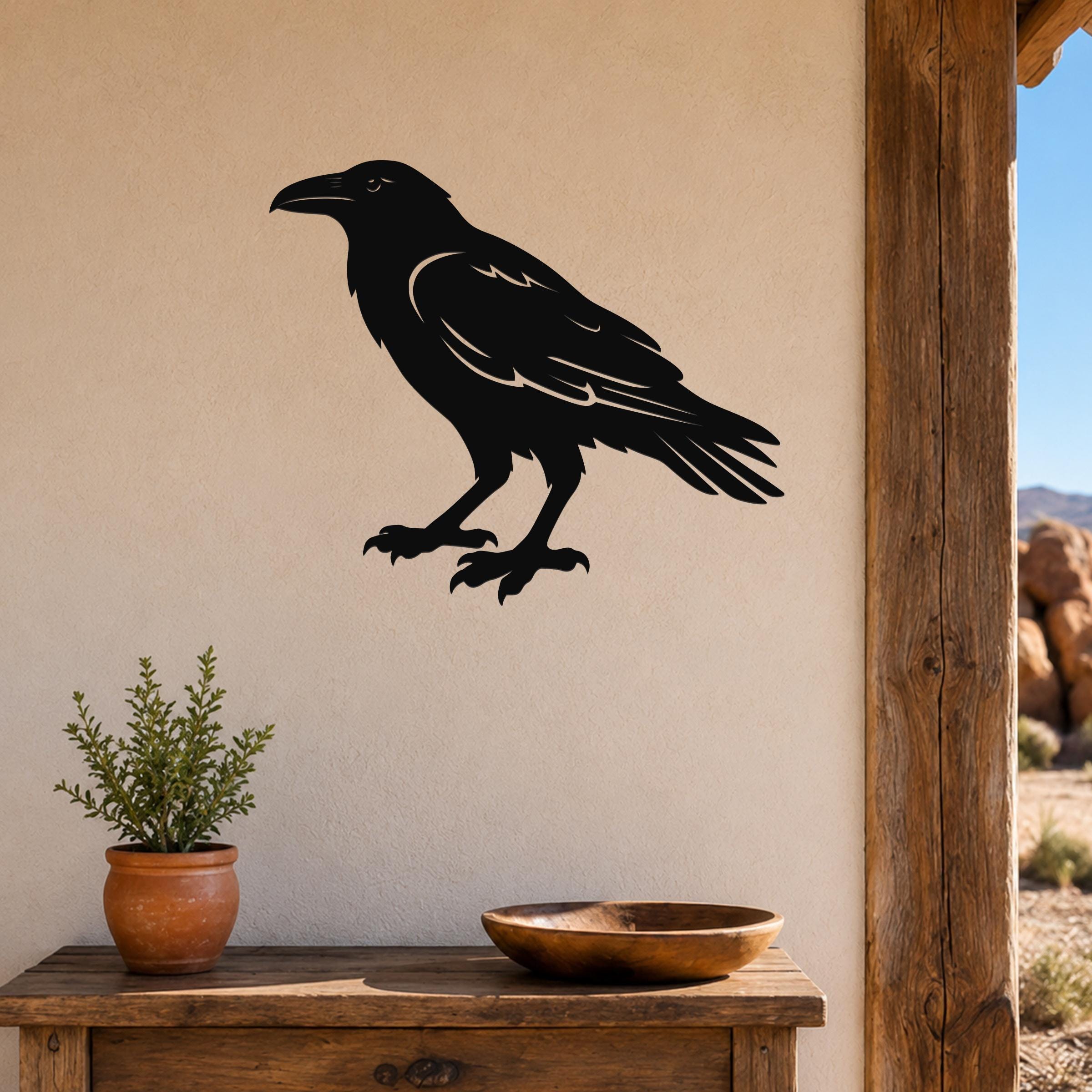 Black metal raven wall art silhouette with detailed feather cutouts, mounted on a beige wall above a wooden table in a rustic outdoor entryway.