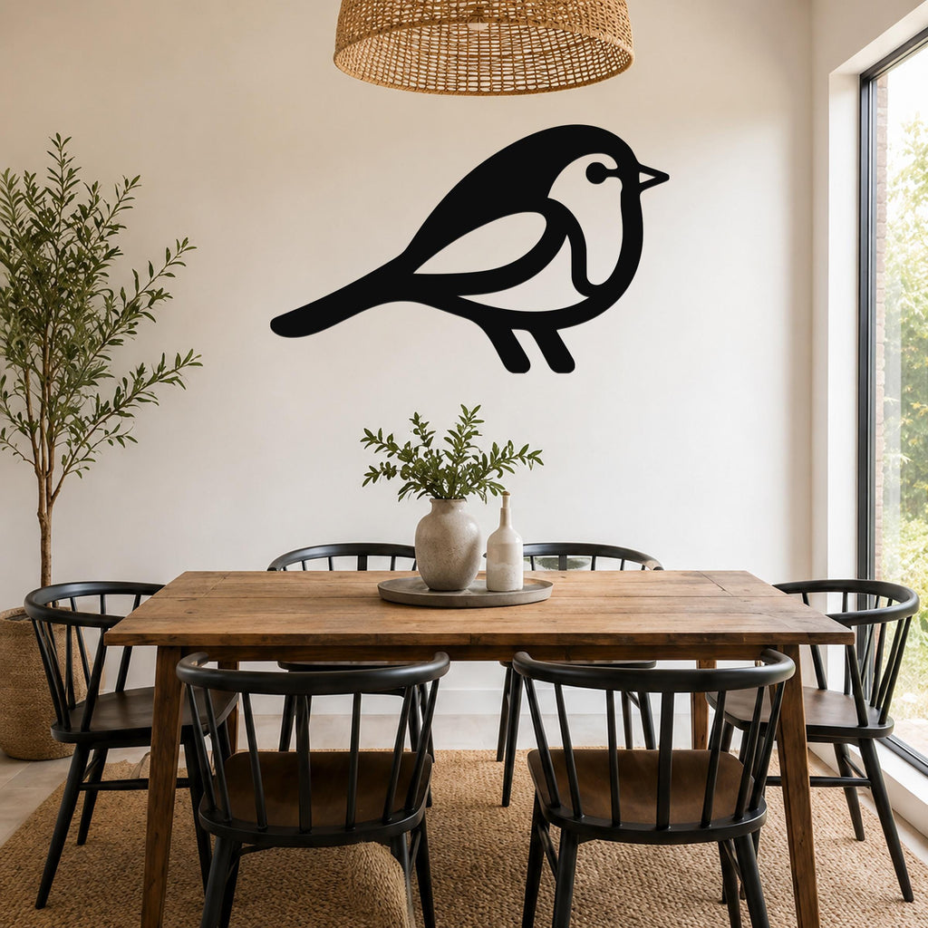 Black metal robin wall art silhouette with internal cutout details, mounted on a white wall above a wooden dining table in a bright dining room.