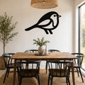 Black metal robin wall art silhouette with internal cutout details, mounted on a white wall above a wooden dining table in a bright dining room.