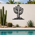 Black metal wall art in the silhouette of a saguaro cactus with branching arms and spines, mounted on a white outdoor wall above a poolside garden.