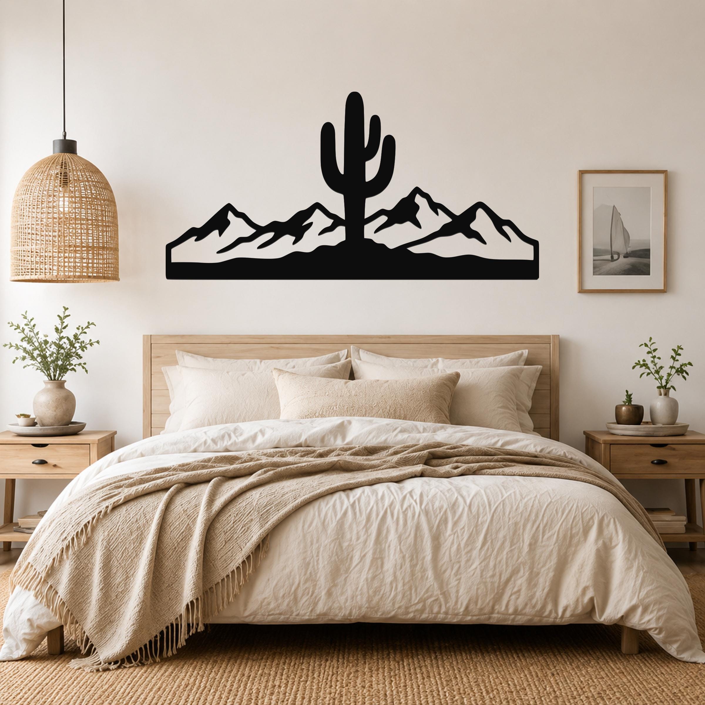 Black metal wall art featuring a saguaro cactus and mountain silhouette, mounted above a bed in a neutral bedroom.