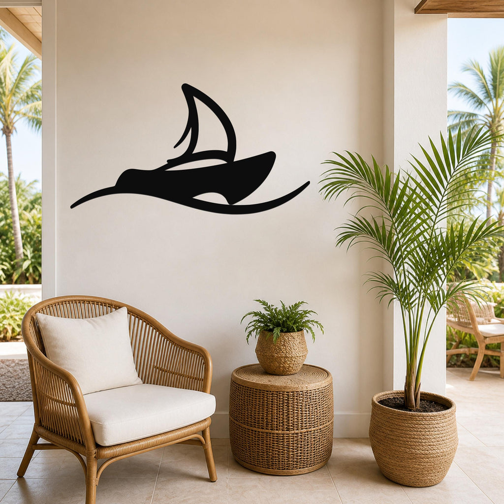 Black metal sailboat wall art with a silhouette design, mounted on a beige wall above a wicker chair in a tropical patio setting.