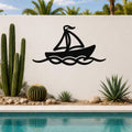 Black metal sailboat wall art with wave cutouts, mounted on a white outdoor wall above a pool with cacti and palm trees in the background.