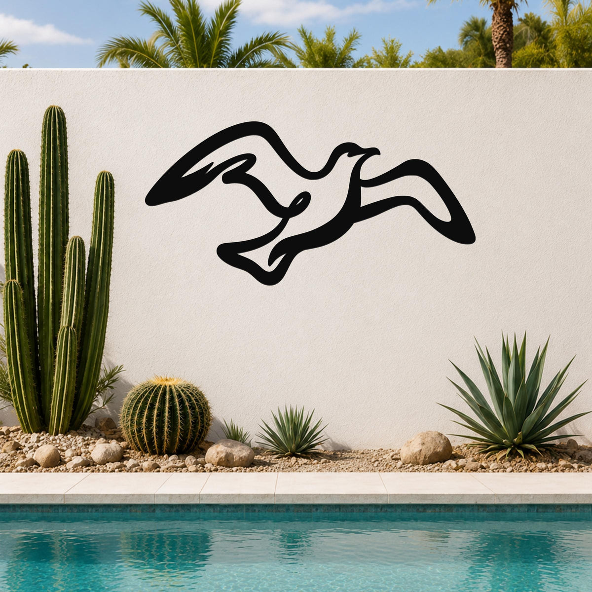 Black metal seagull wall art with flowing silhouette cutouts, mounted on an outdoor wall above a pool with cacti and palm trees in the background.