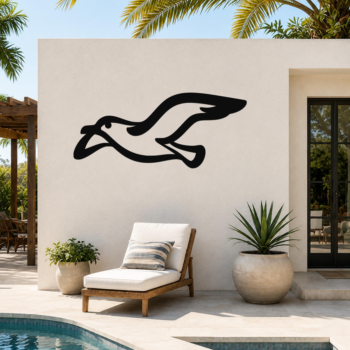 Black metal seagull wall art with a flowing silhouette, mounted on an outdoor patio wall above a lounge chair near a pool.