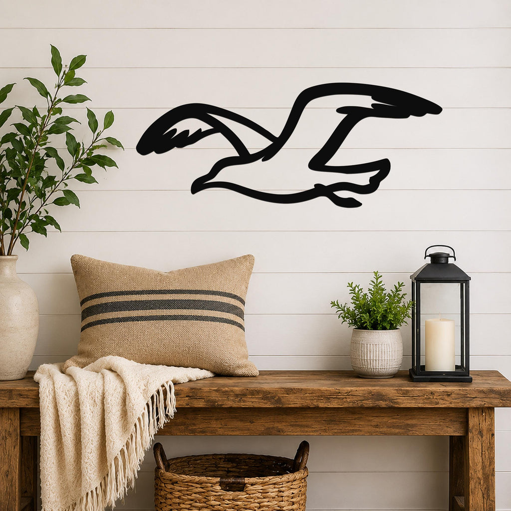 Black metal seagull wall art with motion-line cutouts, mounted above a wooden bench in a coastal living room.
