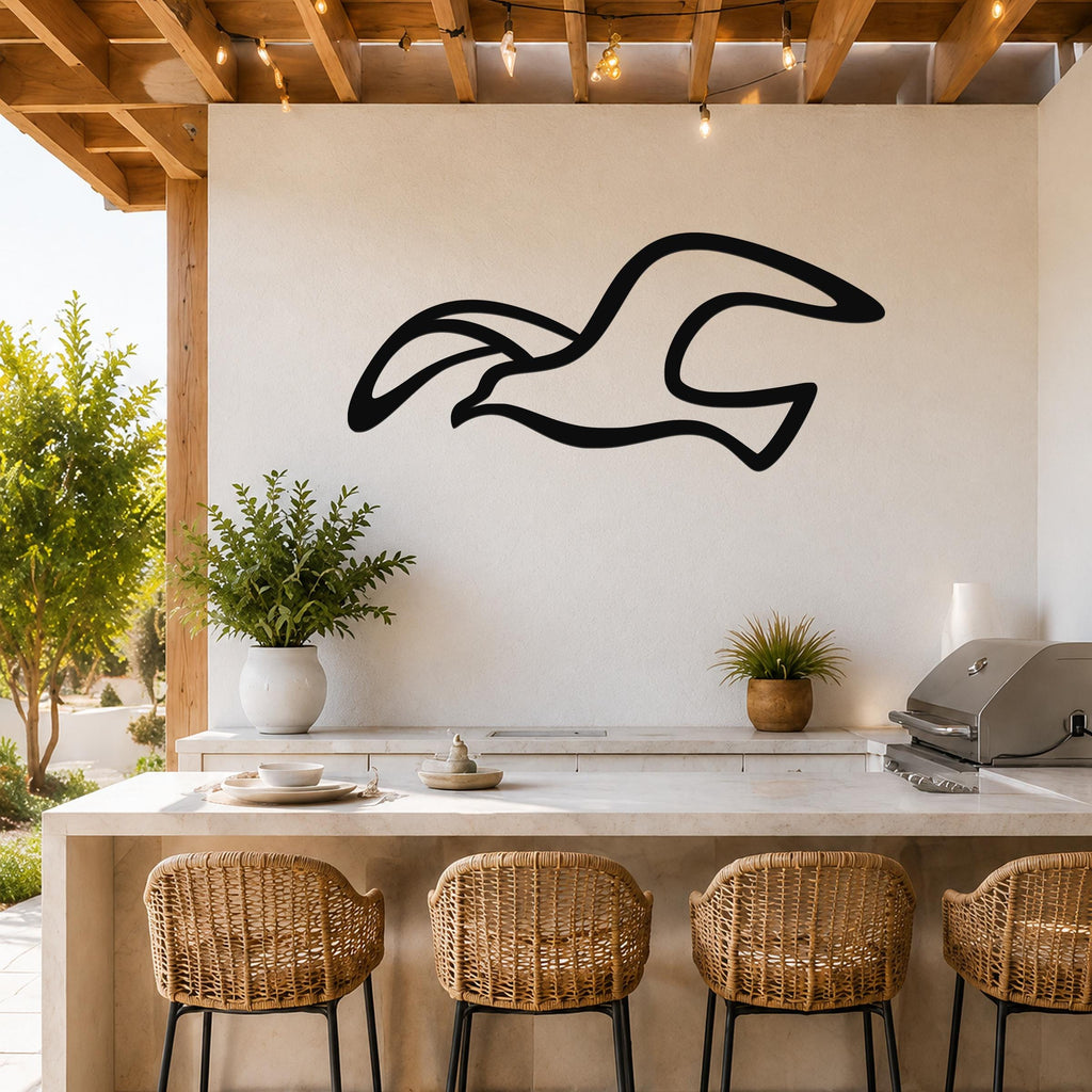 Black metal seagull wall art with flowing silhouette cutout, mounted on a white outdoor kitchen wall above a counter.