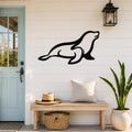 Black metal sea lion wall art with a sleek silhouette design, mounted on a white shiplap wall above a wooden bench in a coastal entryway.