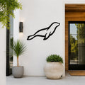 Black metal sea lion wall art silhouette mounted on a white exterior wall beside a glass door and potted plants.