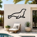 Black metal sea lion wall art in a silhouette style, mounted on an outdoor patio wall above a lounge chair and potted plants.