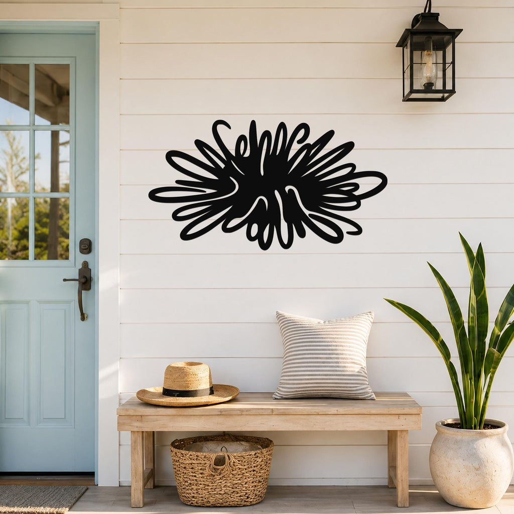 Black metal sea urchin wall art with spiky, radiating cutouts, mounted on a white shiplap wall above a wooden bench in a coastal entryway.