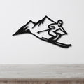 Black metal wall art cutout of a skier in motion with mountain peaks, mounted on a white wall above a light wood surface.
