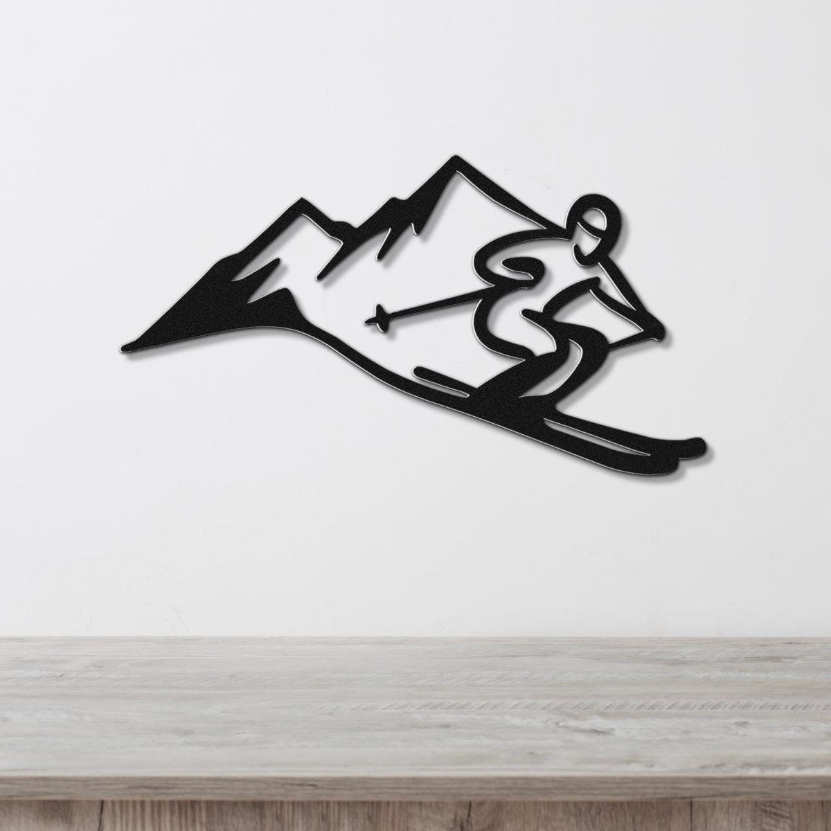 Black metal wall art cutout of a skier in motion with mountain peaks, mounted on a white wall above a light wood surface.