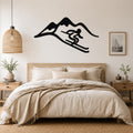 Black metal wall art featuring a skier silhouette in motion against a mountain range, mounted above a wooden bed in a neutral bedroom.