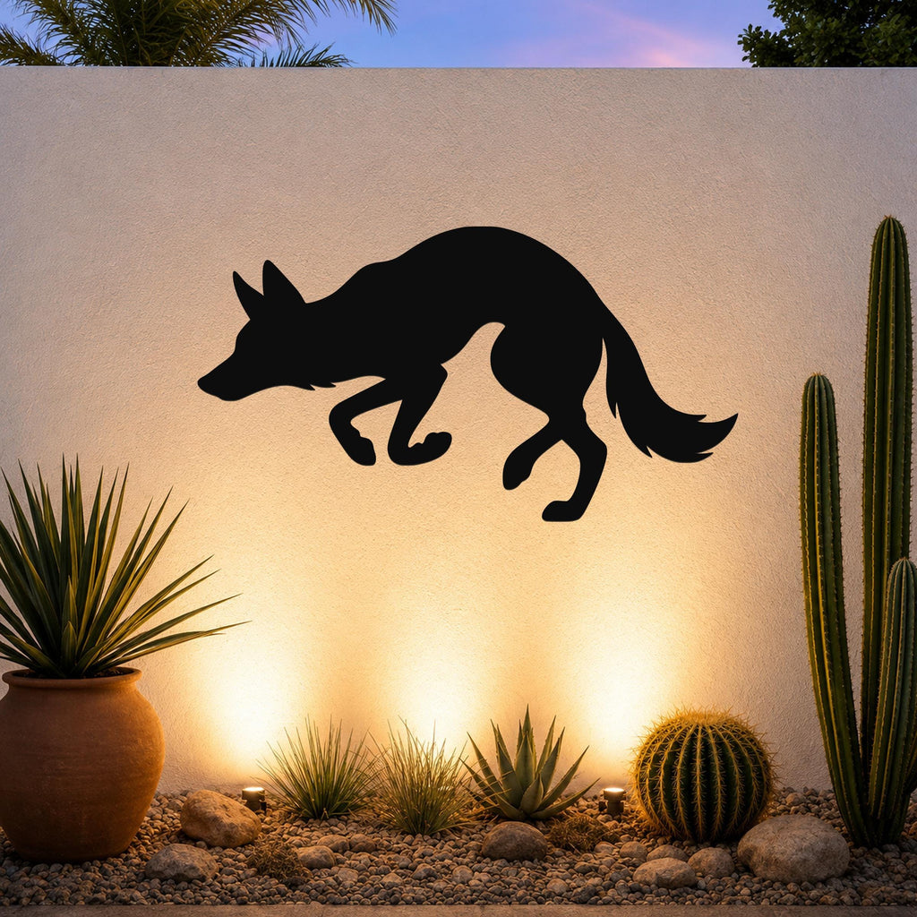 Black metal coyote wall art silhouette mounted on a textured outdoor wall above a desert garden with cacti and warm uplighting.
