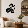 Black metal wall art featuring a coiled snake silhouette with internal cutout patterns, mounted on a living room wall above a white armchair.