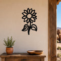 Black metal sunflower wall art with a silhouette design, mounted on a beige wall above a wooden table with a potted plant and bowl.