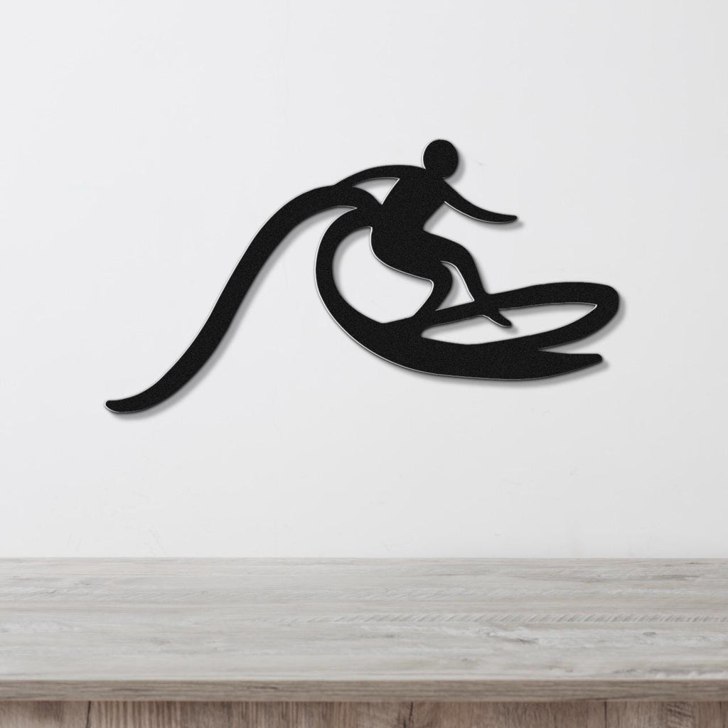 Black metal wall art cutout of a surfer riding a wave, mounted on a white wall above a light wood counter.