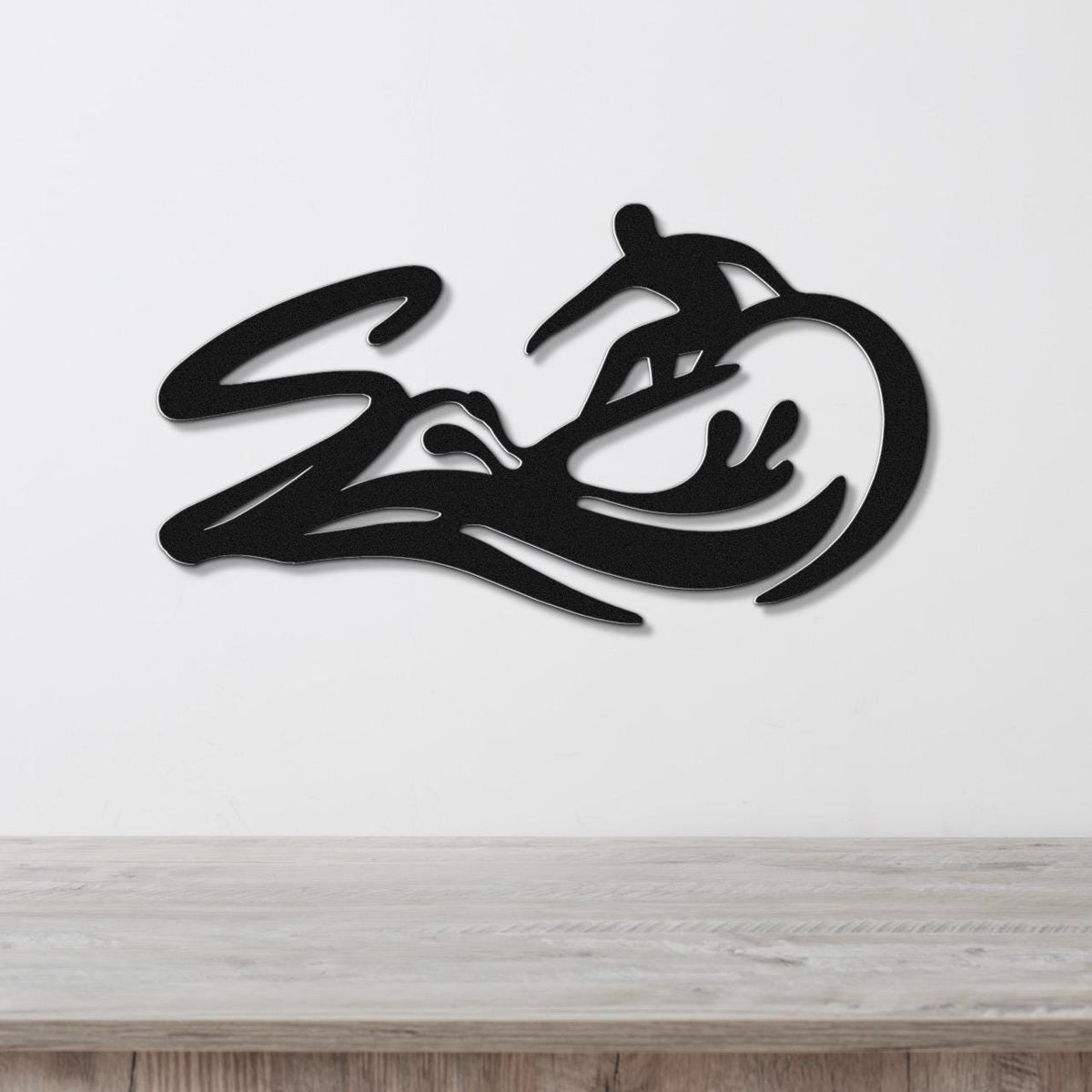 Black metal wall art featuring a surfer silhouette riding a wave, mounted on a white wall above a light wood counter.