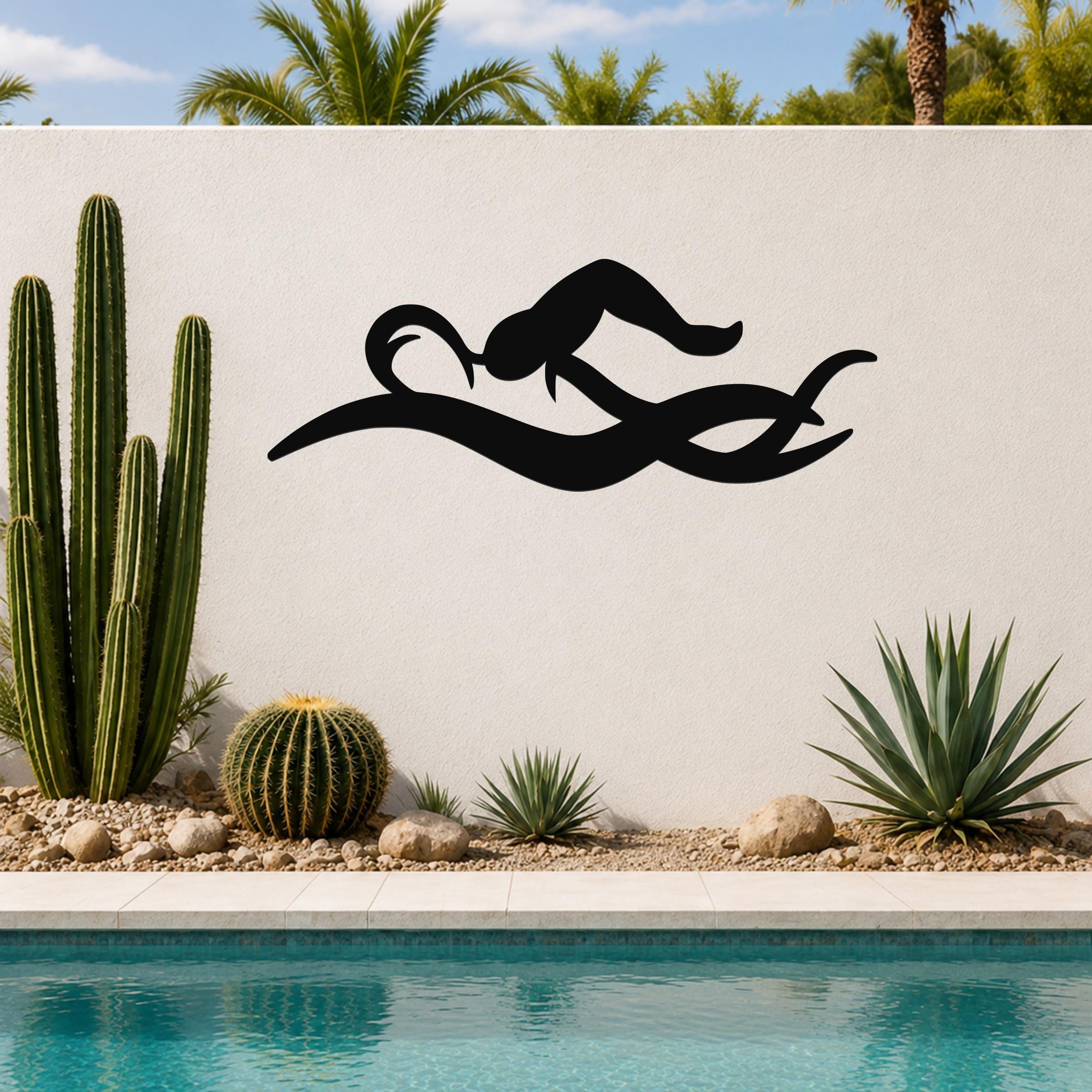 Black metal swimmer wall art with fluid motion cutouts, mounted on a white outdoor wall beside a pool and cacti.