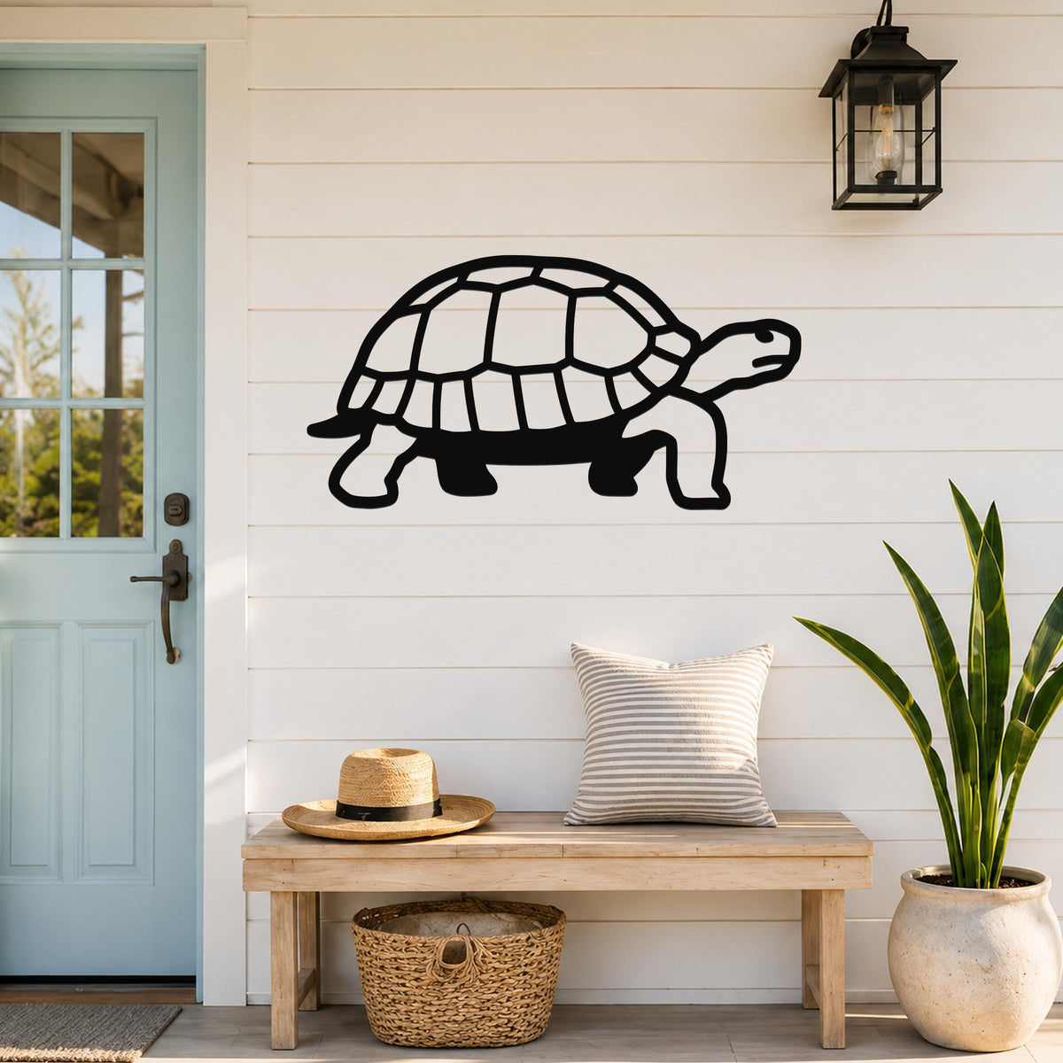 Black metal tortoise wall art with a cutout shell design, mounted on a white shiplap wall above a wooden bench in a front entryway.