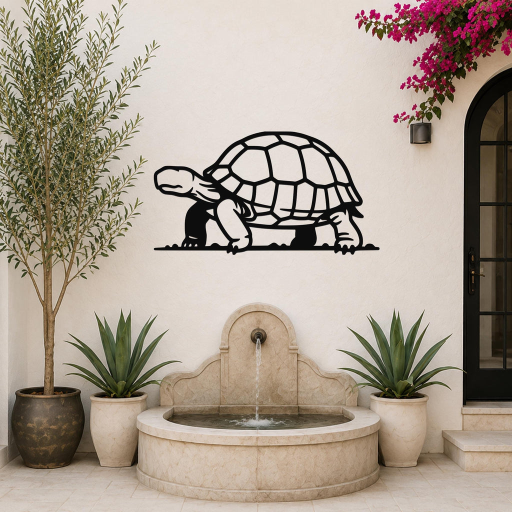 Black metal tortoise wall art with a cutout shell and legs, mounted on a white outdoor wall above a stone fountain.