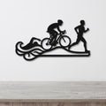 Black metal triathlon wall art with swim, bike, and run silhouettes and motion lines, mounted on a white wall above a wooden surface.