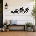 Black metal triathlon wall art with swim, bike, and run silhouettes and motion lines, mounted on a white shiplap wall above a wooden bench on a porch.