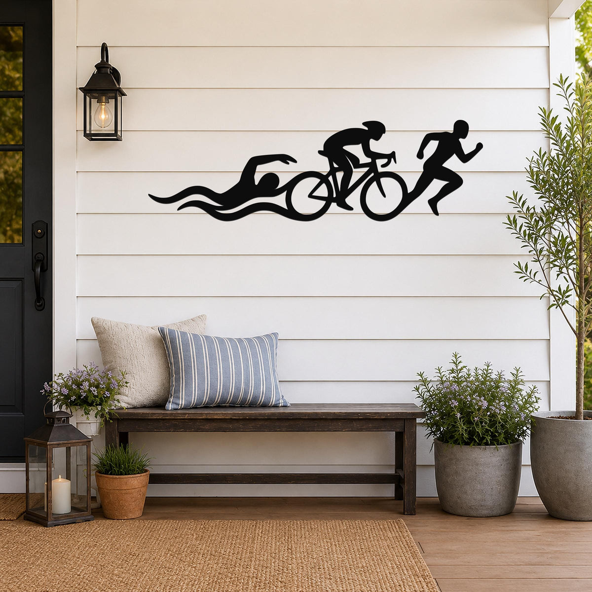 Black metal triathlon wall art with swim, bike, and run silhouettes and motion lines, mounted on a white shiplap wall above a wooden bench on a porch.