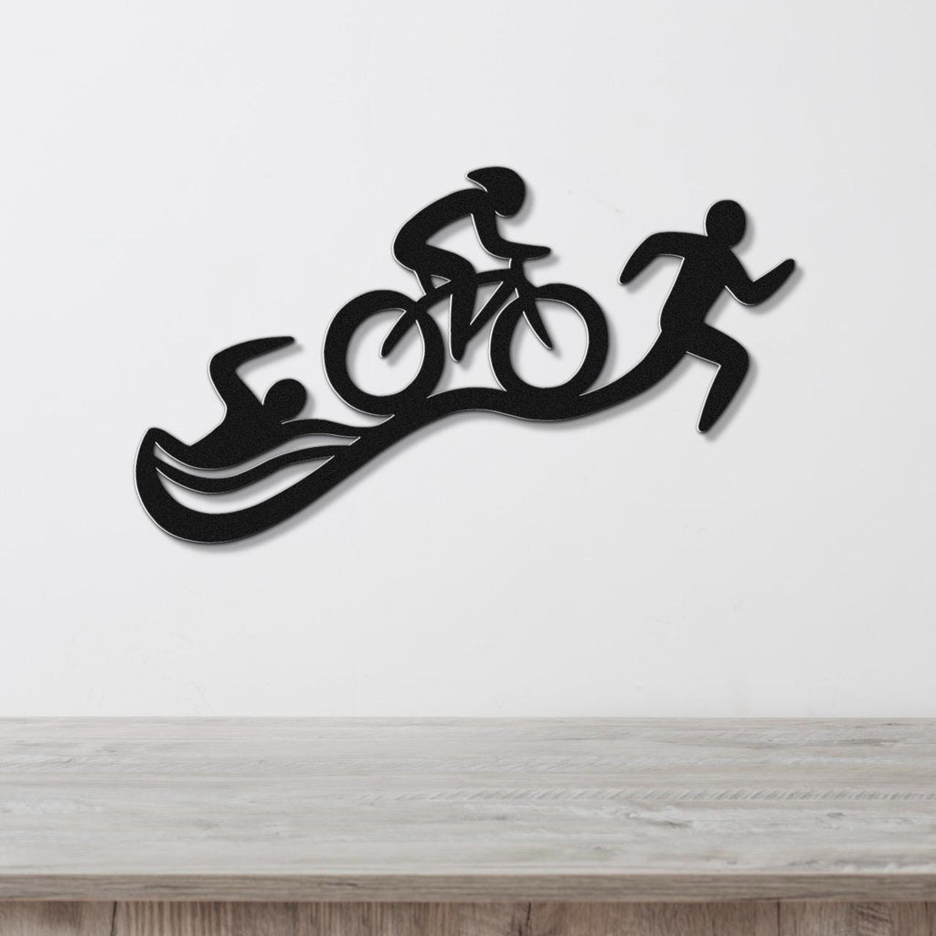 Black metal triathlon wall art with swim, bike, and run silhouettes, mounted on a white wall above a light wood surface.