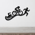 Black metal triathlon wall art with swim, bike, and run silhouettes, mounted on a white wall above a light wood surface.