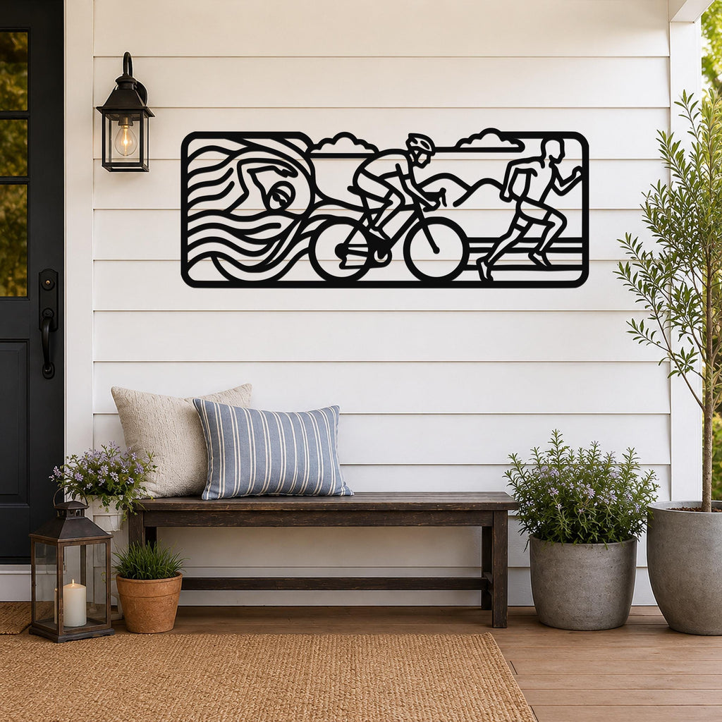 Black metal triathlon wall art with swim, bike, and run silhouettes and motion lines, mounted on a white shiplap wall above a wooden bench on a porch.