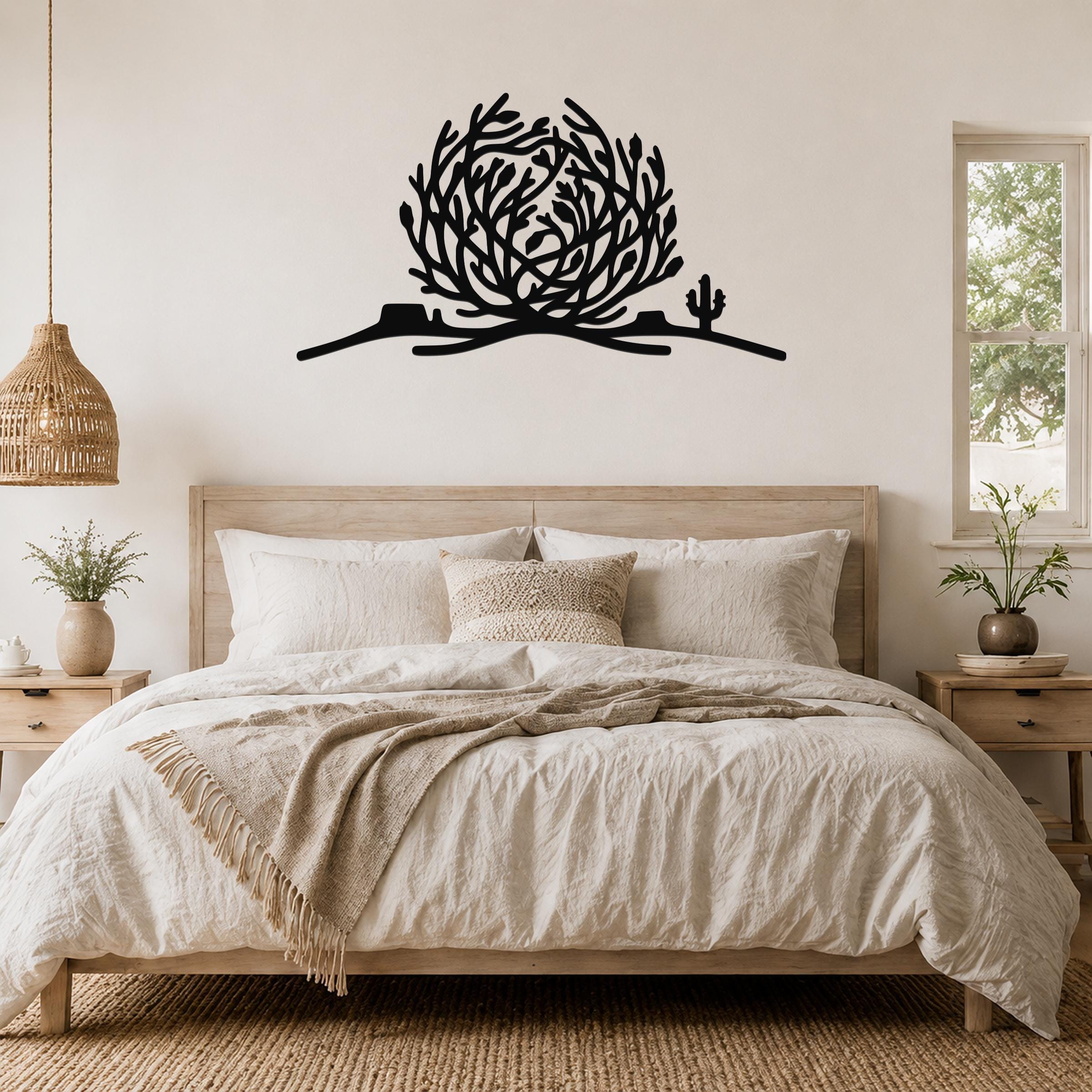 Black metal tumbleweed wall art with cactus silhouette, mounted above a bed in a neutral bedroom.