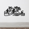 Black metal wall art cutout featuring a triathlon scene with swim, bike, and run silhouettes, palm trees, and waves, mounted on a white wall above a wooden surface.