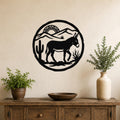Black metal wall art featuring a burro silhouette in a desert scene with cacti and mountains, mounted on a beige wall above a wooden console table.