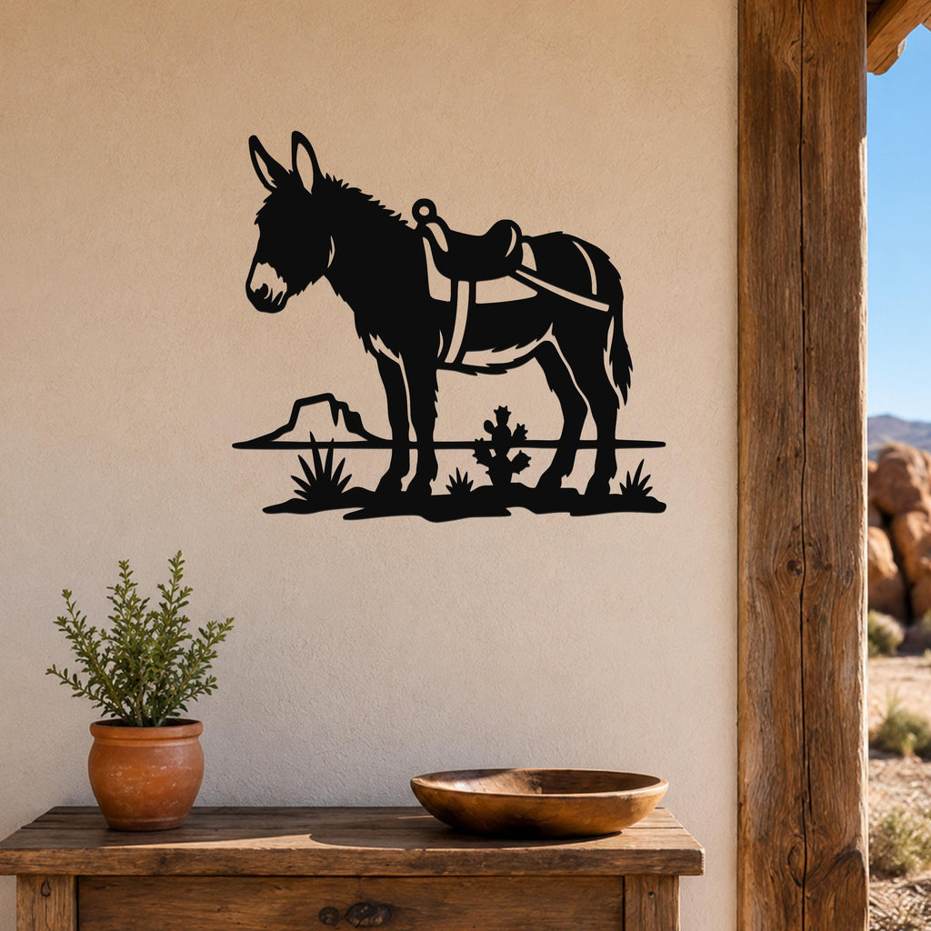 Black metal wall art silhouette of a burro with a saddle, cactus, and rock, mounted on a beige wall above a wooden table in a rustic indoor setting.