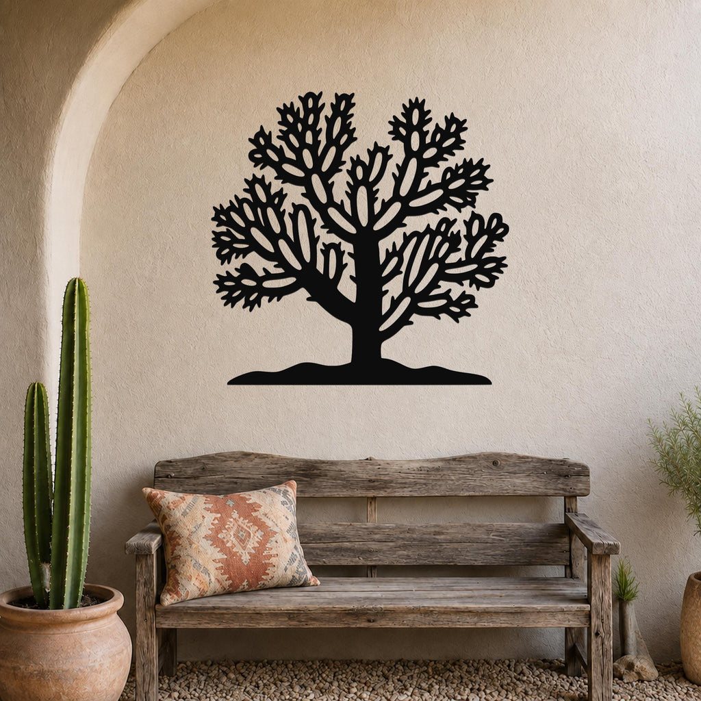 Black metal wall art silhouette of a cholla cactus tree with intricate branching cutouts, mounted on a textured beige wall above a rustic wooden bench in a southwestern-style entryway.