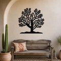 Black metal wall art silhouette of a cholla cactus tree with intricate branching cutouts, mounted on a textured beige wall above a rustic wooden bench in a southwestern-style entryway.