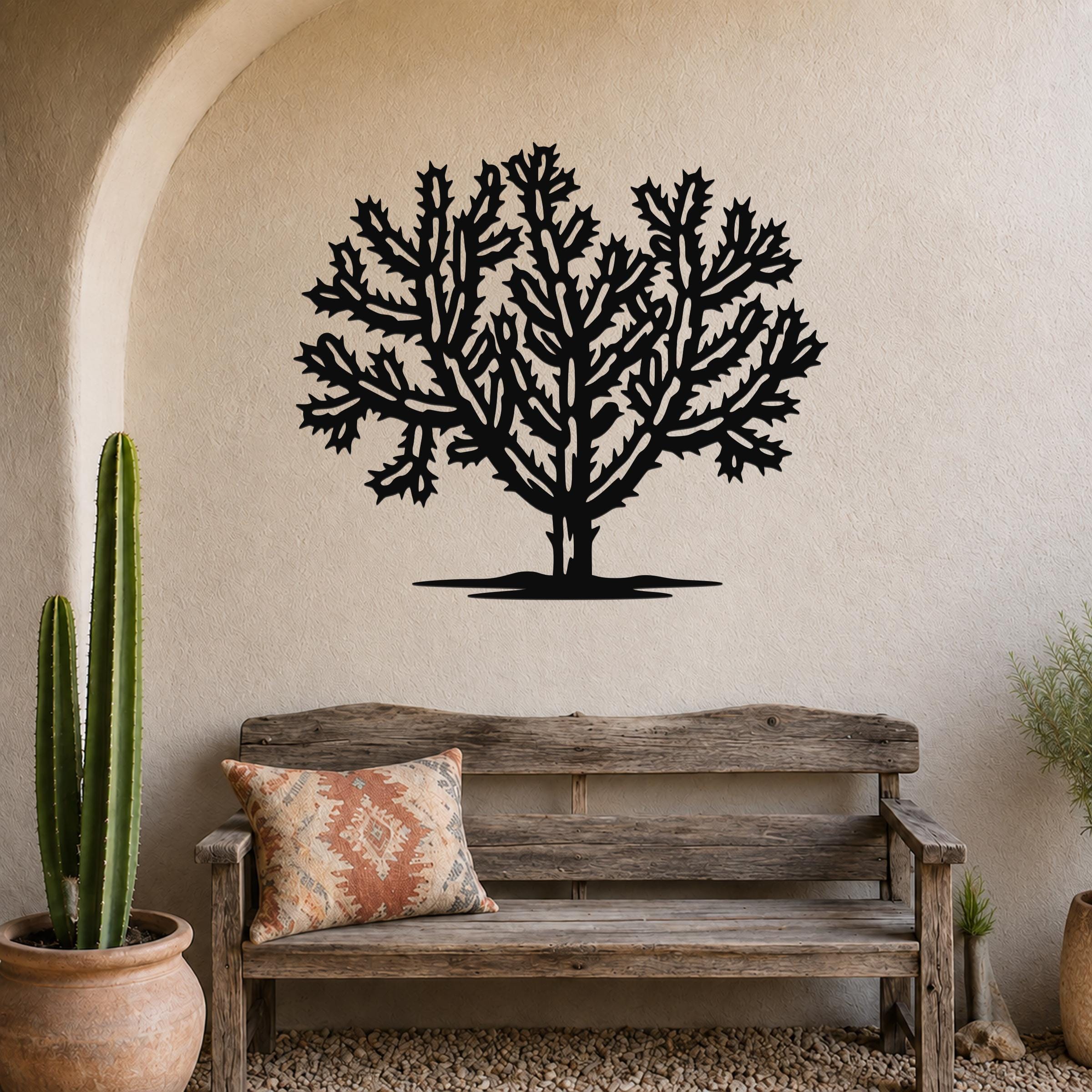 Black metal wall art of a cholla cactus silhouette with intricate branching cutouts, mounted on a textured beige wall above a rustic wooden bench in a southwestern-style entryway.