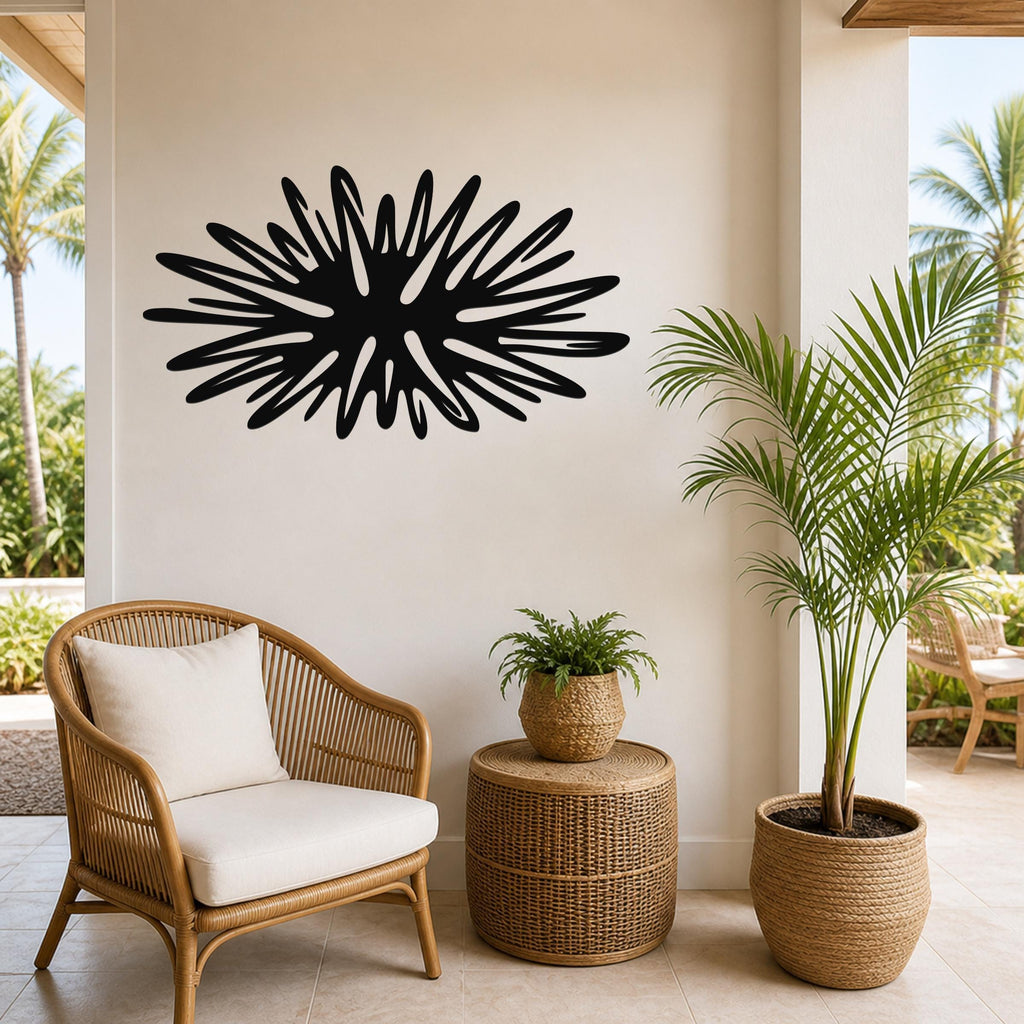 Black metal sea urchin wall art with radiating spines, mounted on a beige wall above a wicker chair in a tropical patio setting.