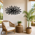 Black metal sea urchin wall art with radiating spines, mounted on a beige wall above a wicker chair in a tropical patio setting.