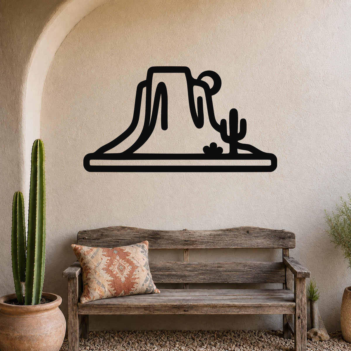 Black metal wall art silhouette of a desert mesa and cactus, mounted on a textured wall above a wooden bench in a southwestern-style entryway.