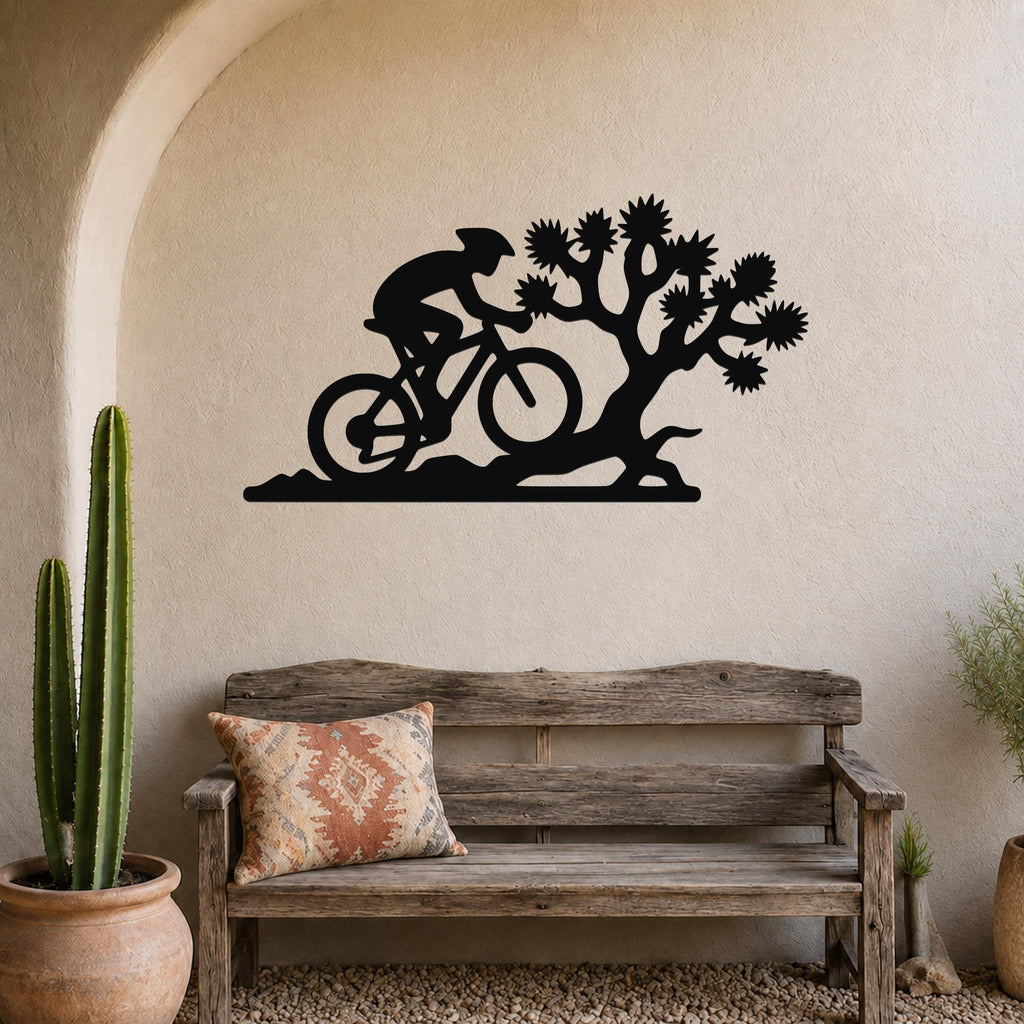 Black metal wall art silhouette of a cyclist and Joshua tree, mounted on a textured wall above a wooden bench in a desert-themed entryway.