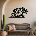 Black metal wall art silhouette of a cyclist and Joshua tree, mounted on a textured wall above a wooden bench in a desert-themed entryway.