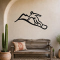 Black metal wall art silhouette of a snowboarder in motion, mounted on a textured beige wall above a rustic wooden bench in a sunlit entryway.