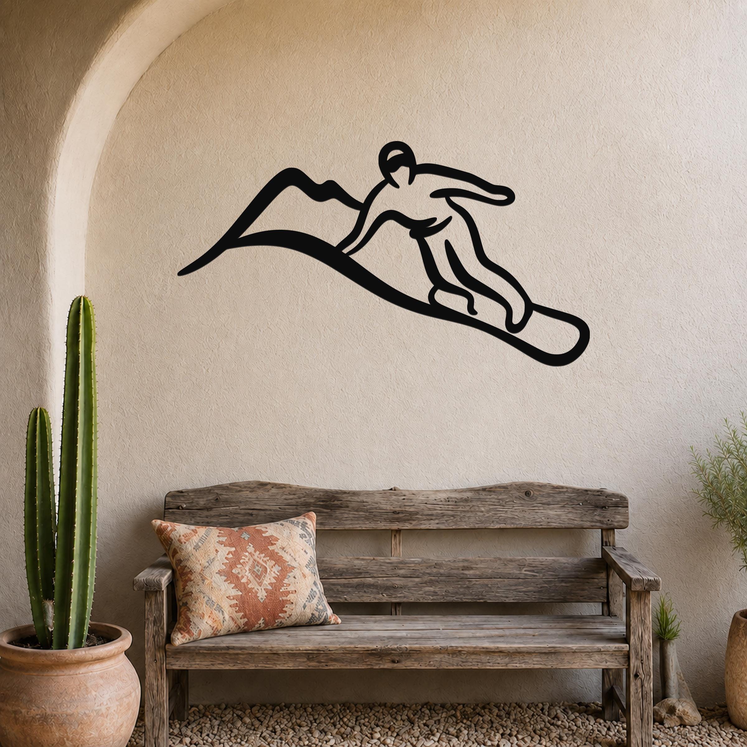 Black metal wall art silhouette of a snowboarder in motion, mounted on a textured beige wall above a rustic wooden bench in a sunlit entryway.