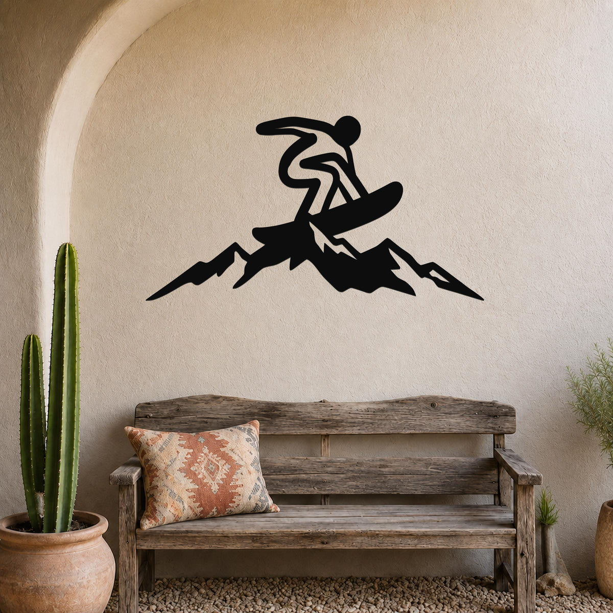 Black metal wall art silhouette of a snowboarder mid-air over mountain peaks, mounted above a wooden bench in a rustic indoor space.