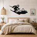 Black metal wall art silhouette of a skier in motion above a bed, mounted on a light-colored bedroom wall.