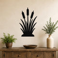 Black metal cattail wall art silhouette with three seed heads and leafy base, mounted on a beige wall above a wooden console table in a living room.