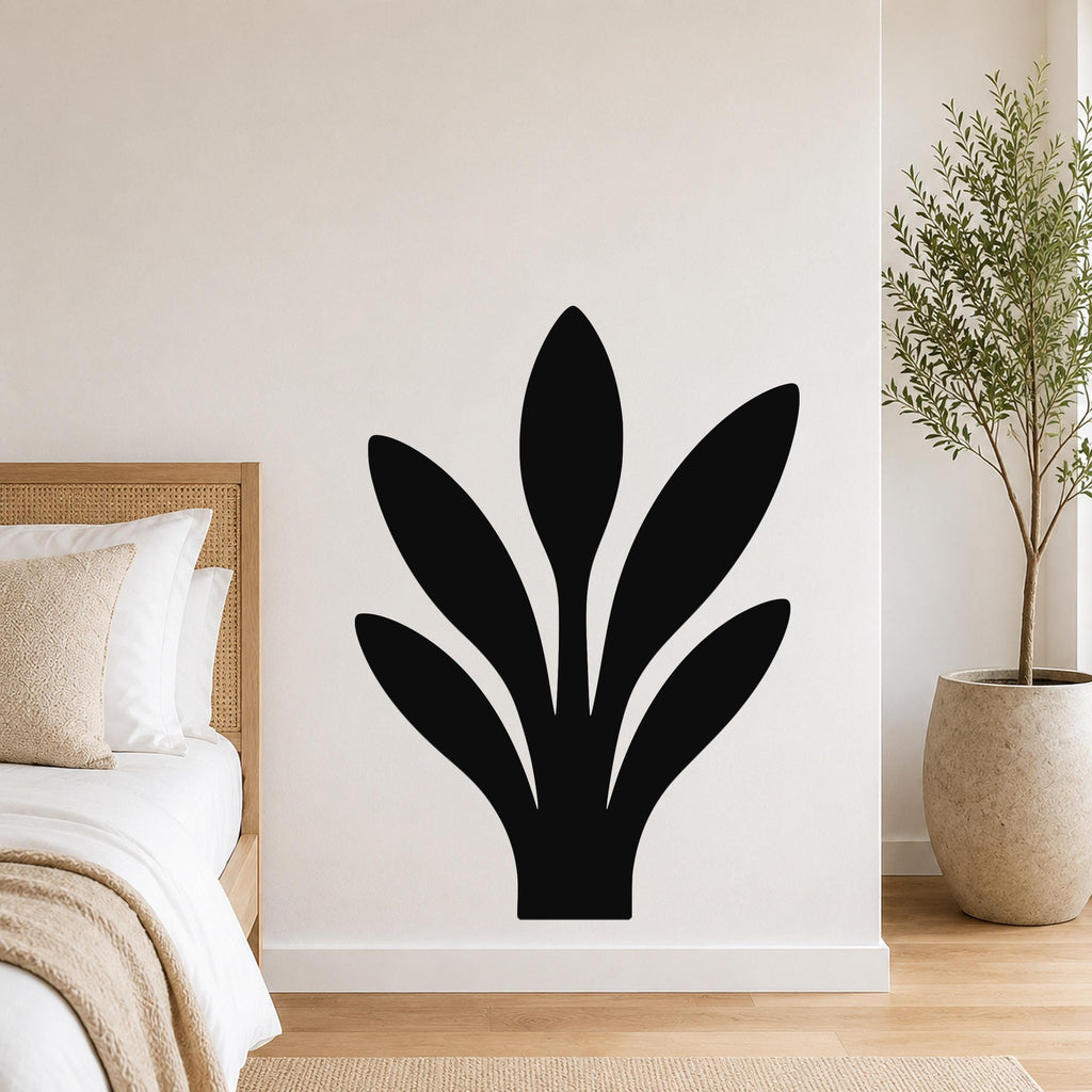 Black metal wall art in a silhouette of a snake plant, mounted on a white bedroom wall above a bed with a woven headboard.
